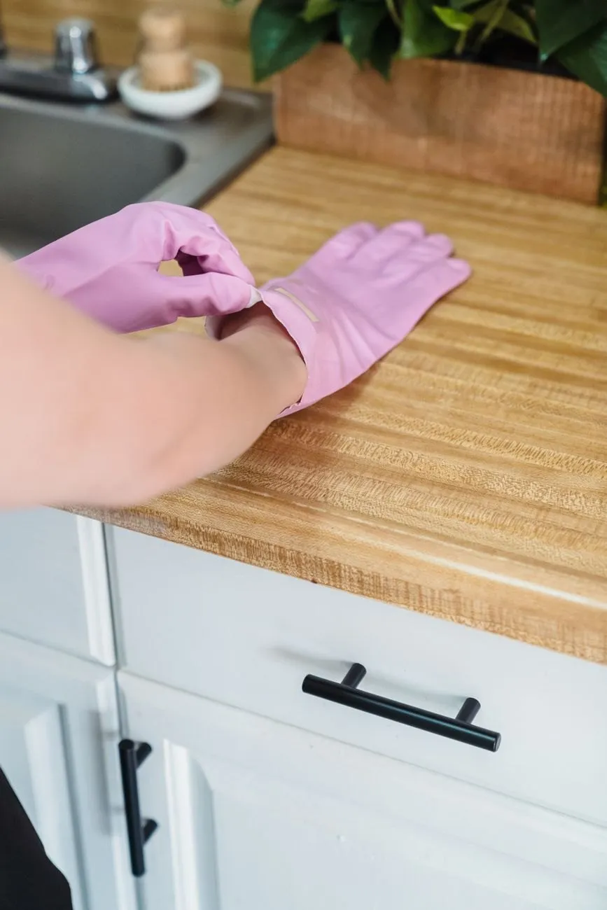 A hand in a pink rubber glove wiping a wooden kitchen worktop