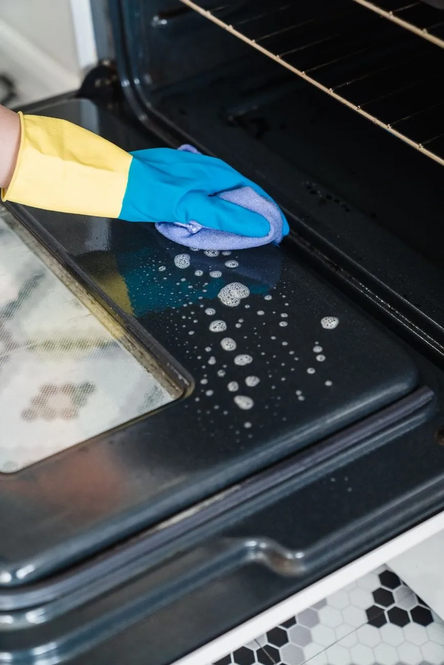 A gloved hand wiping the inside of an oven door with a cloth