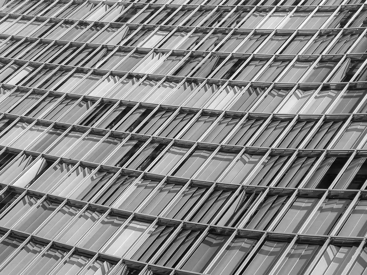 Grid of office glazing seen at an angle, printed achromatic with the specular return at full.